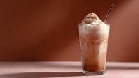 Creamy chocolate milkshake topped with whipped cream and cocoa powder in tall glass against brown background, soft lighting creates appetizing mood.