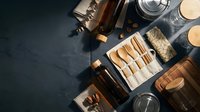 Flat lay composition of luxury skincare and cosmetic products including amber glass bottles, makeup brushes, natural sponges, and candles arranged on dark surface for beauty and wellness branding.
