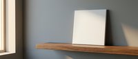 Minimalist wooden shelf with blank white canvas frame against gray wall in modern interior with natural sunlight creating soft shadows for home decor and art display.