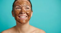 Young woman with chocolate face mask smiling on turquoise background. Skincare beauty treatment spa wellness routine for healthy glowing skin care.