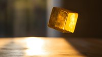 Golden ice cube floating in warm light with glowing translucent effect against blurred background for beverage and cooling concepts.