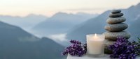 Zen stone stack with burning candle and lavender flowers against misty mountain landscape at sunset for meditation and relaxation practices.
