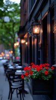 Cozy evening street cafe with glowing lanterns and vibrant red geraniums in window boxes, chairs lined up along facade creating romantic ambiance.