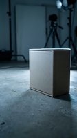 Modern wireless speaker on concrete floor in professional photography studio with equipment and lighting setup in background for audio technology concepts.