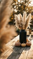 Autumn centerpiece with dried pampas grass in black vase and mini pumpkins on rustic wooden table with warm golden bokeh lights for seasonal decor.