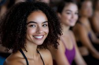 Young African American woman with curly hair smiling during fitness class with diverse group of people exercising together in gym studio.