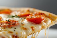 Hot melted cheese stretches from fresh pizza slice with tomatoes and herbs on neutral background for food advertising and restaurant menus.