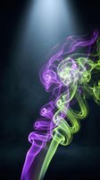Vibrant purple and green smoke swirls rising dramatically against a dark background under a spotlight, creating an abstract, ethereal effect.
