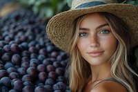 Young woman with straw hat and blonde hair posing near fresh harvested blueberries at farmers market or berry farm during summer season.