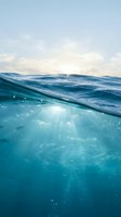 Split underwater ocean view with sunlight rays penetrating clear blue water surface and cloudy sky above for marine and aquatic design projects.