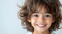 Cheerful young mixed race child with curly brown hair and bright blue eyes showing genuine happy smile against light background. For family, education or healthcare.