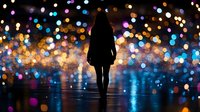 Silhouette of woman standing against colorful bokeh lights background creating magical dreamy atmosphere with reflective surface and glowing defocused spots.