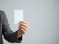 Businessperson in dark suit holding blank white card or paper against neutral gray background, suitable for advertising, marketing campaigns, and corporate messaging.
