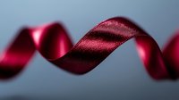 Elegant burgundy silk ribbon curling gracefully against dark background, creating flowing curves and soft shadows. Luxury gift wrapping and decoration element.