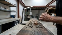 Skilled craftsman carving intricate wooden relief sculpture in workshop using traditional hand tools and techniques for artisan woodworking projects.