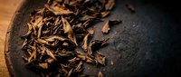 Dried tobacco leaves scattered on dark surface, close-up shot showing texture and detail for smoking product advertising and agricultural content.