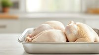Raw whole chickens in metal baking pan on white kitchen counter, showing fresh poultry texture and natural color in bright daylight setting.