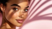 Young mixed race woman with glowing skin and natural makeup in warm sunlight with palm leaf shadow overlay creating soft pink tones and artistic lighting effect.