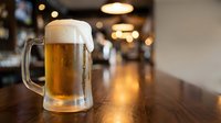 Fresh draft beer mug with foam on wooden bar counter in modern pub restaurant with warm ambient lighting for hospitality industry marketing.