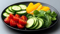 Fresh sliced vegetables and greens arranged on black plate including cucumber, yellow peppers, cherry tomatoes and baby spinach leaves for healthy eating.