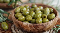 Fresh green olives in rustic wooden bowl with olive branches, Mediterranean appetizer on natural background, close up view of traditional food.
