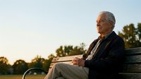 Senior Caucasian man in dark jacket sitting peacefully on park bench during golden hour sunset, contemplating life with serene expression outdoors.