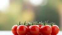 Fresh red cherry tomatoes on vine with water droplets arranged in row on white surface against blurred natural background for cooking and healthy eating.