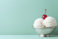 Three scoops of vanilla ice cream in a silver bowl topped with a cherry, on a mint green background with copy space.