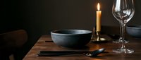 Elegant table setting with blue ceramic bowl, burning candle, wine glass, and utensils on wooden surface for fine dining and restaurant concepts.