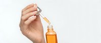 Woman hand holding glass dropper bottle with golden serum oil for skincare routine and beauty treatment on white background.