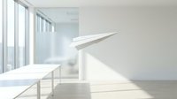 White paper airplane flying in bright modern office space with natural sunlight streaming through large windows onto wooden floor.