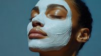Young African American woman with closed eyes wearing white facial mask against blue background, wellness and skincare concept for spa and beauty advertising.
