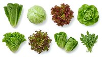 Fresh assorted lettuce and leafy greens isolated on white background, including romaine, iceberg, red leaf and butter lettuce varieties for salad preparation and healthy eating.