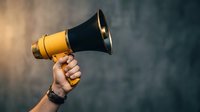 Hand holding yellow and black megaphone against blurred background for communication, announcement, marketing campaigns and public speaking concepts.