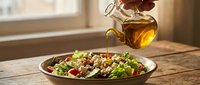 Salad bowl with mixed greens, vegetables, and nuts on wooden table with olive oil being drizzled from bottle, suitable for food, nutrition, and healthy eating content.