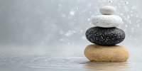 Balanced zen stones stacked on water surface with bokeh background, creating peaceful spa atmosphere for wellness and meditation concepts.