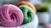 Colorful yarn skeins in pink, green, and orange arranged on soft knitted fabric, showcasing texture and warmth for crafting projects.