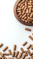 Brown herbal supplement capsules in wooden bowl on white background for health and wellness marketing materials.