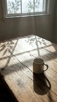 Ceramic mug on wooden floor with natural sunlight streaming through window, casting shadows from foliage. Minimalist interior scene for lifestyle and wellness content.