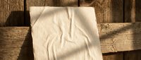 White crumpled paper napkin on rustic wooden crate surface with natural lighting and shadows creating texture contrast for eco-friendly packaging design concepts.