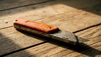 Vintage woodworking chisel with worn wooden handle resting on rustic wooden planks in natural sunlight for carpentry and craftsmanship projects.