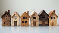 Row of miniature wooden houses with rustic texture and varying natural wood tones standing on white surface, showcasing handcrafted architectural details.