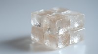 Translucent ice cubes stacked in minimalist composition on light background create soft shadows and reflections, showcasing crystalline texture and purity.