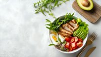 Healthy protein bowl with grilled chicken, avocado, egg, fresh vegetables and greens on light background, balanced nutrition meal.