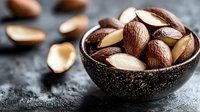 Mixed nuts in rustic bowl on dark stone surface with scattered almonds and brazil nuts for healthy snacking and cooking ingredients.