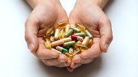Hands holding assorted vitamin capsules and supplements in gold and green colors against white background for healthcare and wellness concepts.