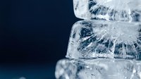 Ice cubes stacked with crystalline texture and frost formations against dark blue background, suitable for beverage, refreshment and cooling concept designs.