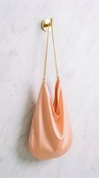 Peach satin hobo bag with gold chain strap hanging on a brass hook against a white marble wall, elegant fashion accessory.