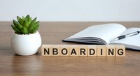 Wooden letter blocks spelling ONBOARDING on desk with open notebook, pen and small succulent plant in white pot for business training concepts.