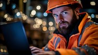 Professional construction worker with safety helmet using laptop computer at industrial site with bokeh lights background for engineering projects.